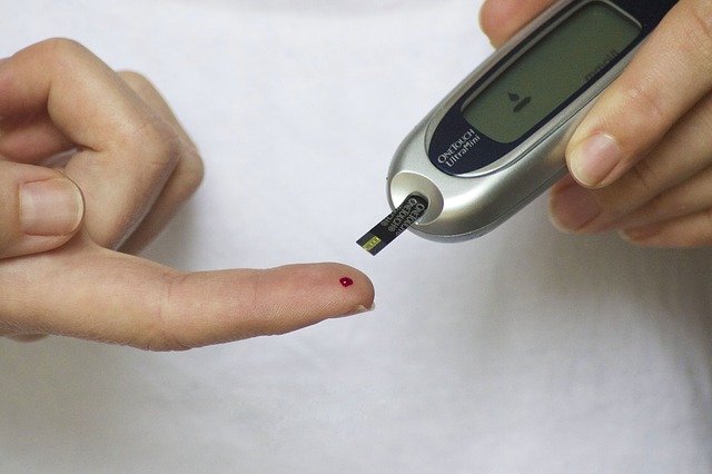 A blood glucose test strip attached to a device is held near a droplet of blood on a fingertip.