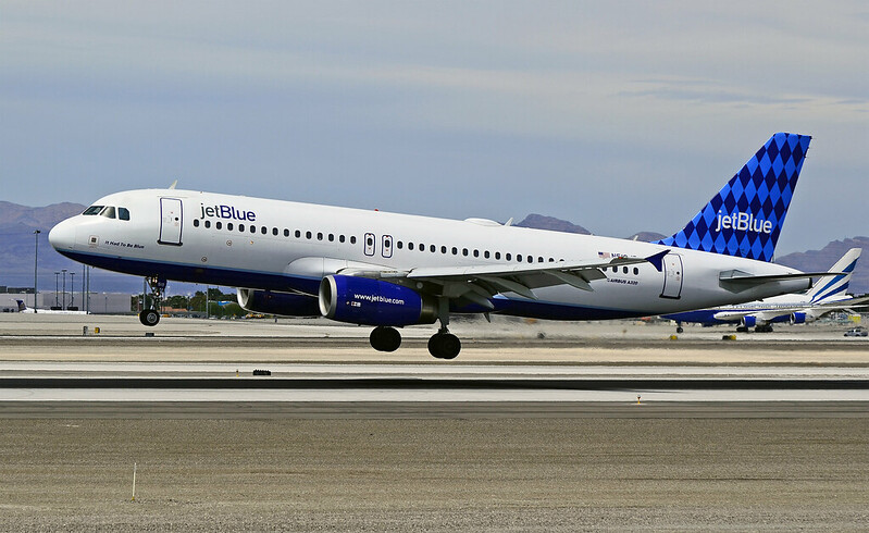 A passenger jet in JetBlue livery with its landing gear extended about to land on a runway.
