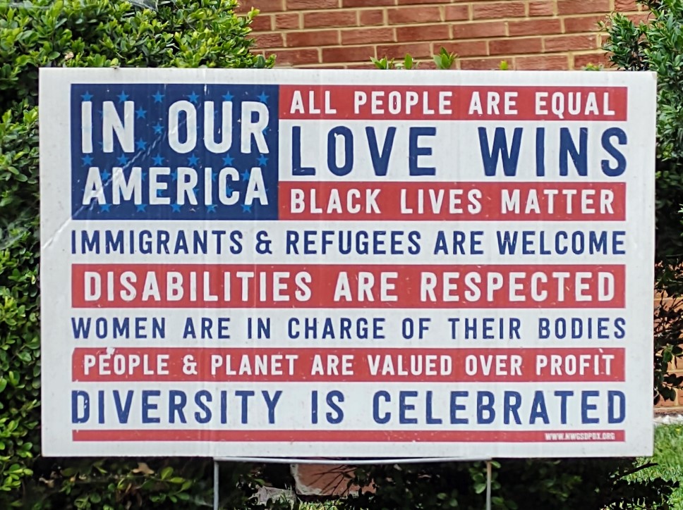 A lawn sign that contains a United States flag, but with various slogans superimposed upon it.