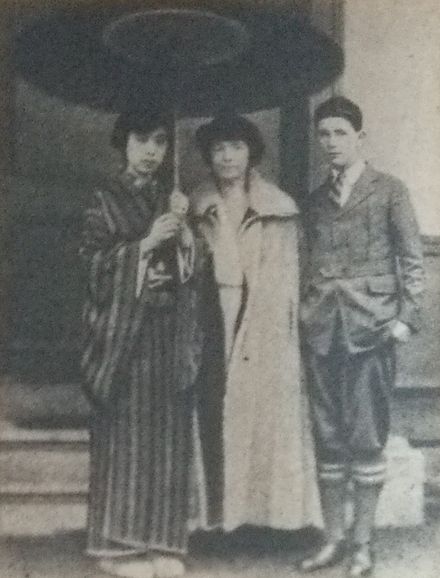Ishimoto Shizuko holds a parasol that she shares with Margaret Sanger, who stands next her. On the other side of Margaret Sanger is her son Grant, who has his hands in his pockets.