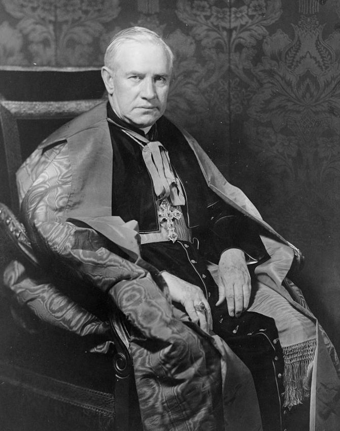 Patrick J. Hayes sits in a chair, wearing clergical robes and a cape.