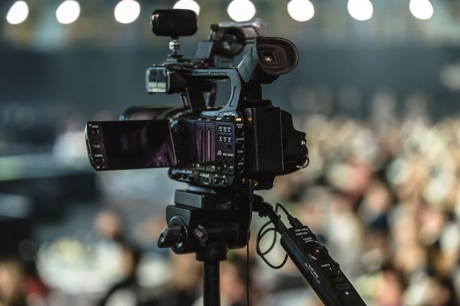 A close-up of a video camera at an event, with camera in focus and the background blurred.